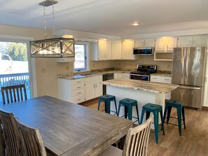 A modern kitchen with white cabinets, a stainless steel refrigerator, a microwave, and a stove. There is a wooden dining table with four blue bar stools.