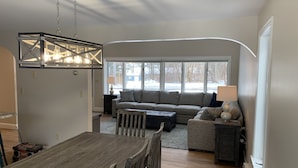 Ein modernes Wohnzimmer mit Essbereich, großen Fenstern und einer Kronleuchter.