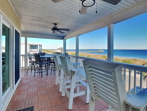 A covered outdoor area with a table and chairs, a ceiling fan, and a view of the beach and ocean.