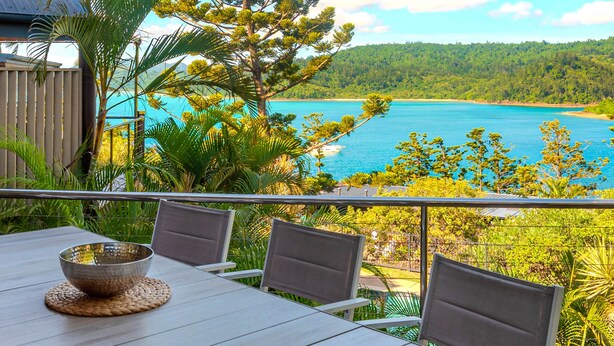 A balcony with a table, chairs, and a view of a coastal landscape. - Cooinda Gardens 1, Beautiful Apartment on Hamilton Island (Hamilton Island)