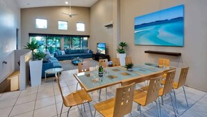 A spacious living area with a glass dining table, comfortable seating, a large TV, and a scenic painting on the wall. - Cooinda Gardens 1, Beautiful Apartment on Hamilton Island (Hamilton Island)
