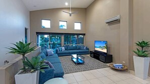A modern living room with a sectional sofa, a flat-screen TV, and a ceiling fan. - Cooinda Gardens 1, Beautiful Apartment on Hamilton Island (Hamilton Island)