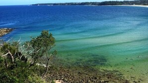 A coastal view with clear blue waters, a sandy beach, and some greenery. - ABSOLUTE Mollymook BEACHFRONT- Direct beach access  and views / Wifi / Smart TV  (Mollymook Beach)