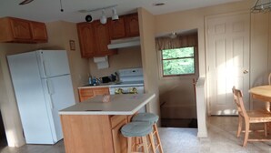 A compact kitchen with a central island, wooden cabinets, a refrigerator, and a dining area with a table and chairs. -  Rest and relax- great view of Hemlock hills and surrounding area.  (Hemlock)