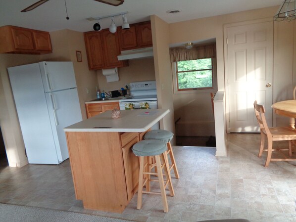 A compact kitchen with a central island, wooden cabinets, a refrigerator, and a dining area with a table and chairs.