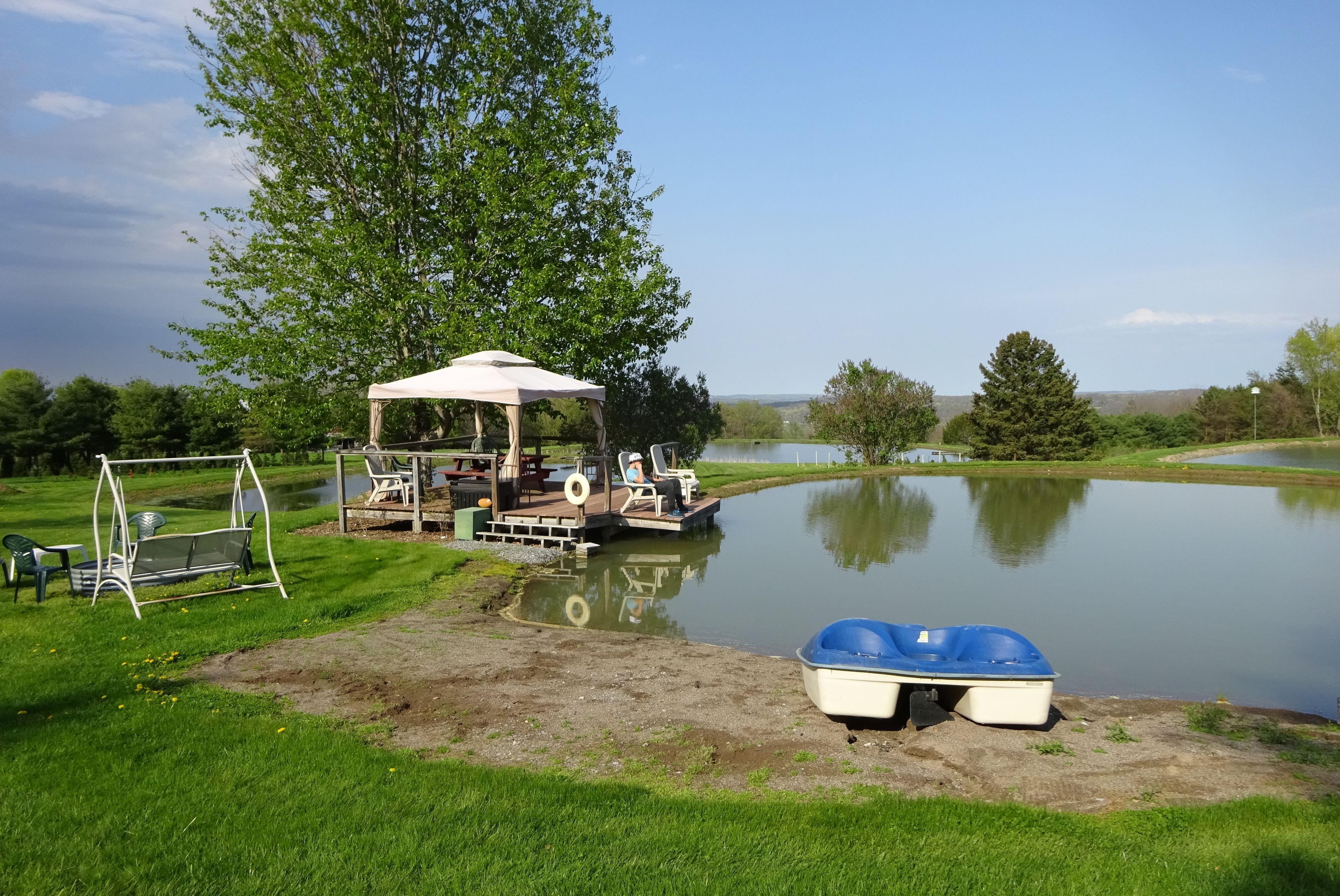 A serene lakeside setting with a gazebo, a swing set, and a small boat docked near the shore.