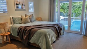 Een slaapkamer met een bed, een nachtkastje, een lamp en uitzicht op een zwembad door een glazen deur.