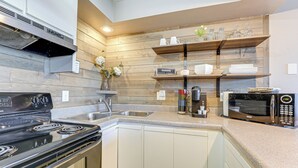 A modern kitchen with a stainless steel stove, a microwave, and wooden shelves above the counter. - 2 Mi to Silver Dollar City: Condo in Branson West (Reeds Spring)