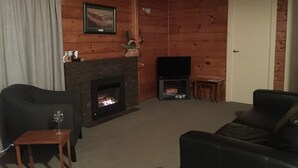 A cozy living room with a fireplace, a television, and leather sofas. - Tui Glen - Lake front bach with stunning views (Lake Tarawera)