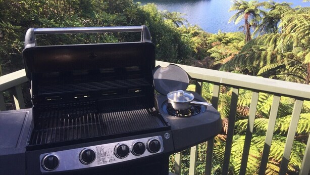 A grill on an outdoor balcony with a view of a lake and trees. - Tui Glen - Lake front bach with stunning views (Lake Tarawera)
