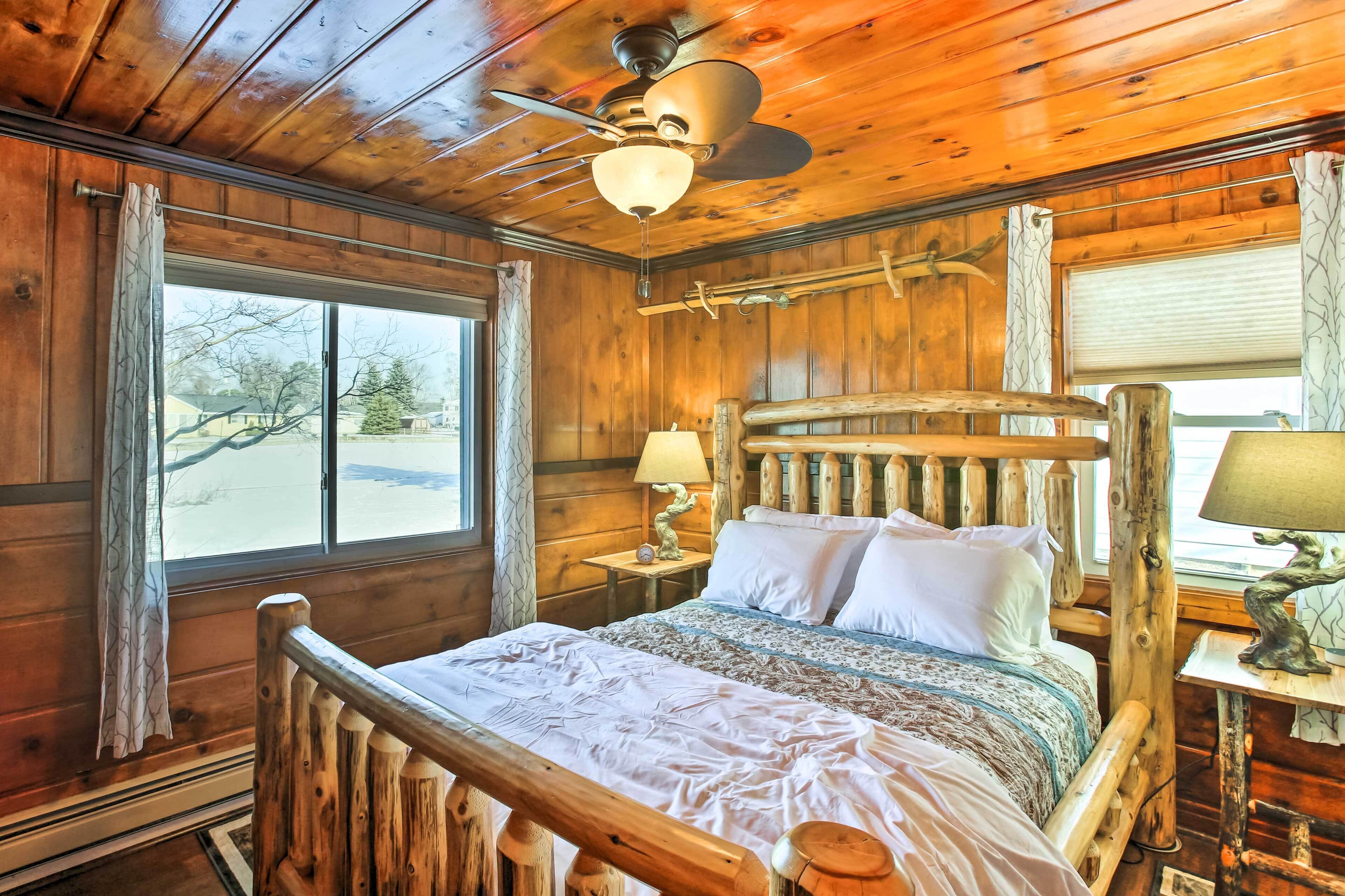 A wooden cabin bedroom with a bed, a ceiling fan, and a window with curtains.