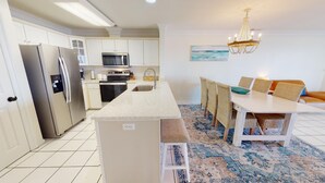 Una cocina moderna con electrodomésticos de acero inoxidable, una isla central y un comedor con sillas de mimbre y una mesa.