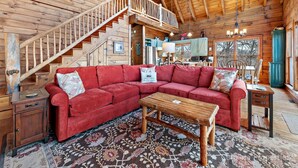 Un intérieur de chalet chaleureux avec un canapé d’angle rouge, une table basse en bois et un escalier menant à un niveau supérieur.