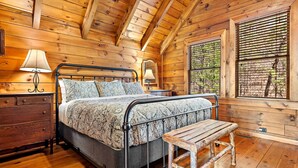 Une chambre dans une cabane en bois, avec un lit, des lampes de chevet, un banc et une fenêtre avec des stores.
