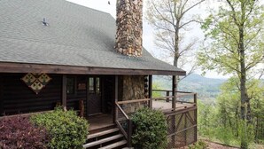 Une cabane en rondins avec une cheminée en pierre, une véranda en bois et une vue sur la forêt environnante.