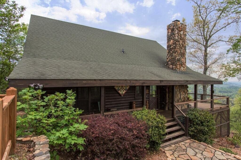 A log cabin with a stone chimney, wooden deck, and a stone pathway leading to the entrance.