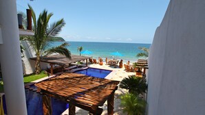 A pool area with a wooden deck, lounge chairs, and umbrellas, overlooking a beach and ocean.