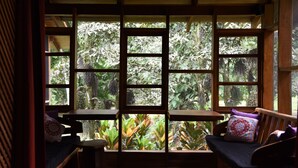 A room with a large window divided into multiple panes, wooden furniture, and a view of dense foliage outside. - Las Casas Costa Rica a private lodge in the Caribbean jungle (Cocles)