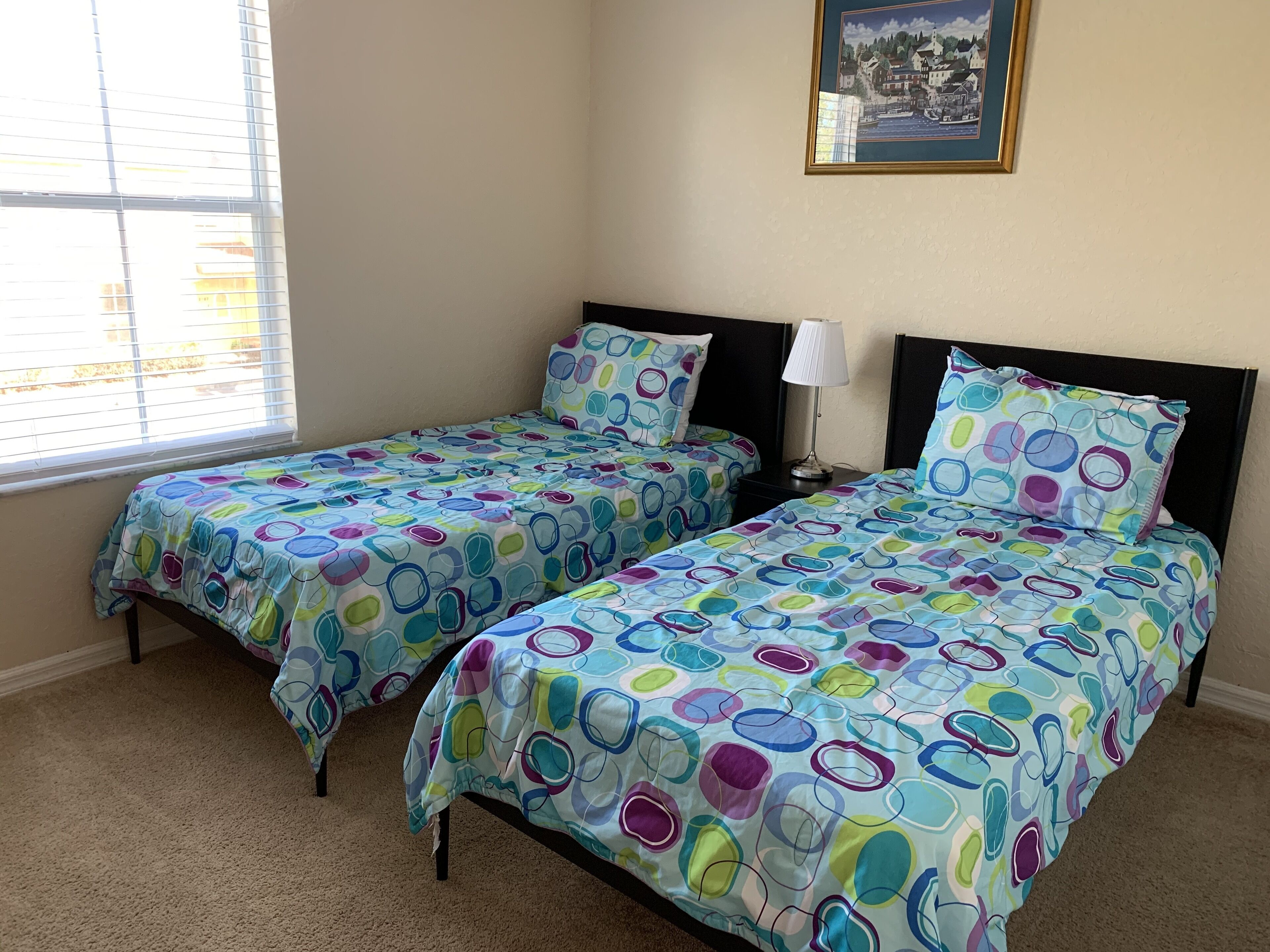 A bedroom with two beds, a nightstand, a lamp, and a framed picture on the wall.