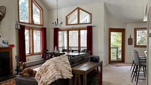 Een ruime woonkamer met een open haard, een eettafel en een groot raam met uitzicht op een terras.