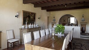 A dining room with a large wooden table, white upholstered chairs, a decorative centerpiece, and a painting on the wall.