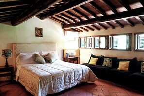 A bedroom with a bed, a sofa, a small table, and a picture on the wall.