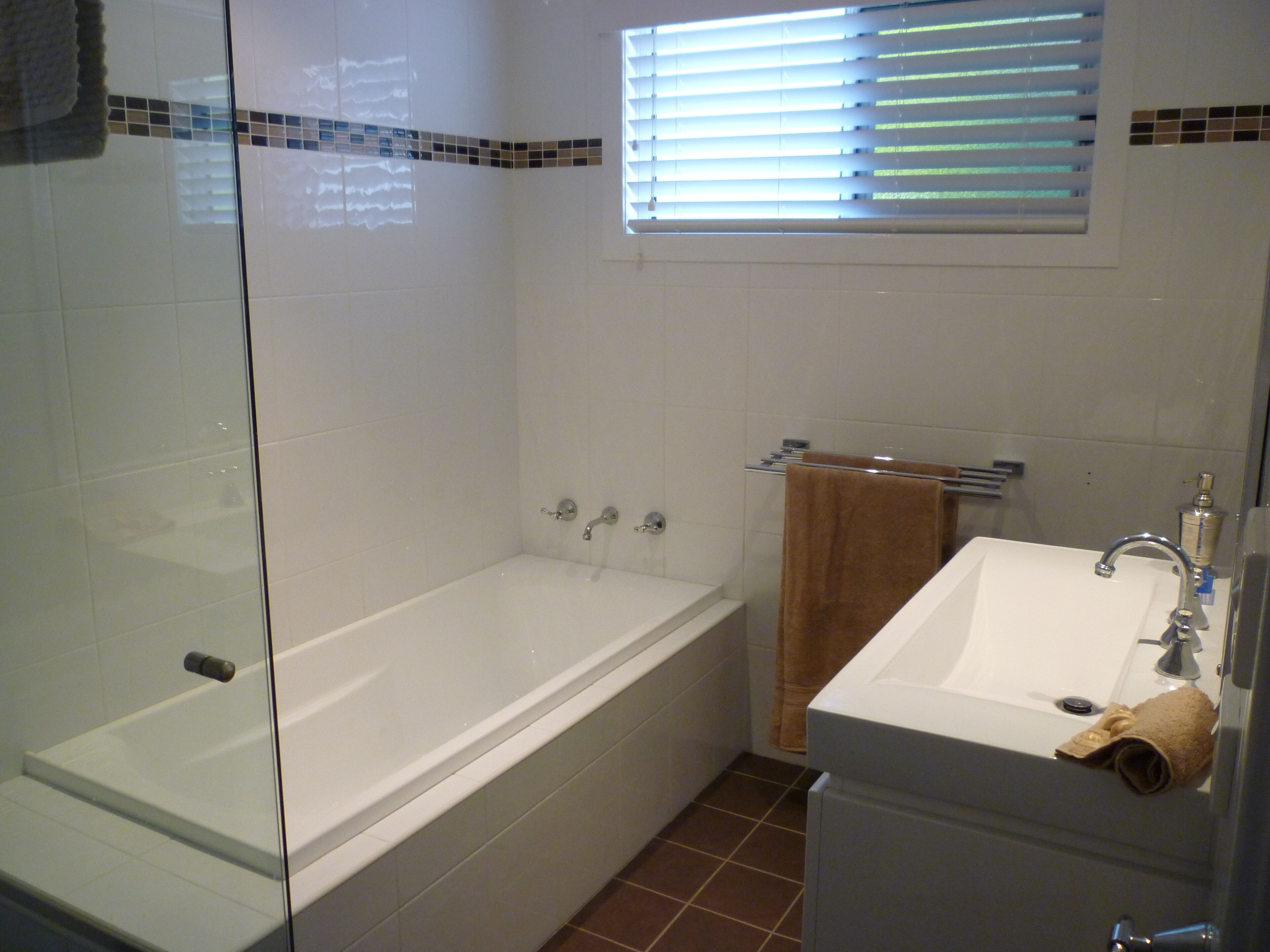 A bathroom with a glass-enclosed shower, a white bathtub, and a sink with a towel hanging on the wall.