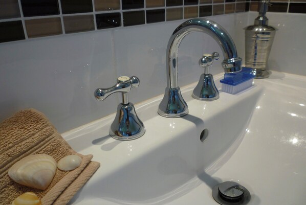 A bathroom sink with two chrome faucets, a soap dish, and a blue toothbrush holder. - Bannister Blu (Mollymook)