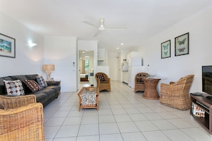 A spacious living area with a sofa, wicker chairs, a coffee table, and a television.