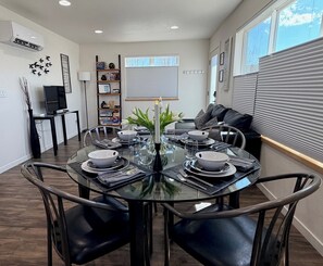 Un coin repas avec une table ronde en verre, dressée pour quatre personnes, entourée de chaises en cuir noir.