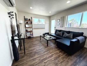 A living room with a black leather sofa, a glass coffee table, a bookshelf, and a large window. - Modern Carriage House in Prospect - America's Coolest Neighborhood (Longmont)