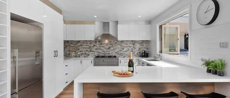 A modern kitchen with a central island, stainless steel appliances, and a large window.