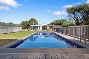 A rectangular swimming pool with a wooden deck in the foreground, surrounded by a wooden fence.
