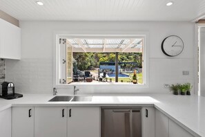 A modern kitchen with a built-in dishwasher, a window overlooking a pool area, and a wall-mounted clock.