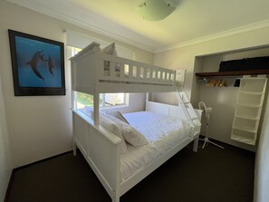 A bunk bed room with a window, a fan, and a shelf with hanging clothes.