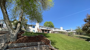 Un jardin arrière d’une maison, aménagé avec un foyer en pierre, un banc en bois et une pelouse bien entretenue.