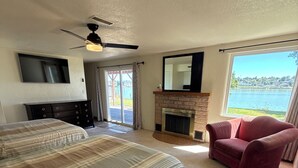 Une chambre avec un grand lit, une cheminée, une télévision et une vue sur un lac.