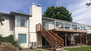 Une maison moderne dotée d’un balcon en verre, d’un escalier en bois et d’un grand arbre en arrière-plan.