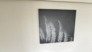 Une table à manger en bois, accompagnée de quatre chaises grises à revêtement rembourré, une assiette de nourriture et une œuvre d'art représentant une fougère accrochée au mur.
