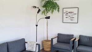 Un salon moderne avec deux canapés gris, une lampe sur pied, une plante en pot et une œuvre d’art représentant un poisson, encadrée et accrochée au mur.