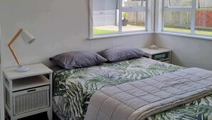 Une chambre à coucher avec un lit, une table de chevet, une lampe et une fenêtre donnant sur l’extérieur.