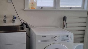 Une petite buanderie équipée d’un lave-linge à chargement frontal, d’un évier et d’une fenêtre située au-dessus du lave-linge.