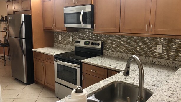 A kitchen with wooden cabinets, stainless steel appliances, a microwave, an oven, and a granite countertop. - Cozy and Charming Condo in Naples (Naples)