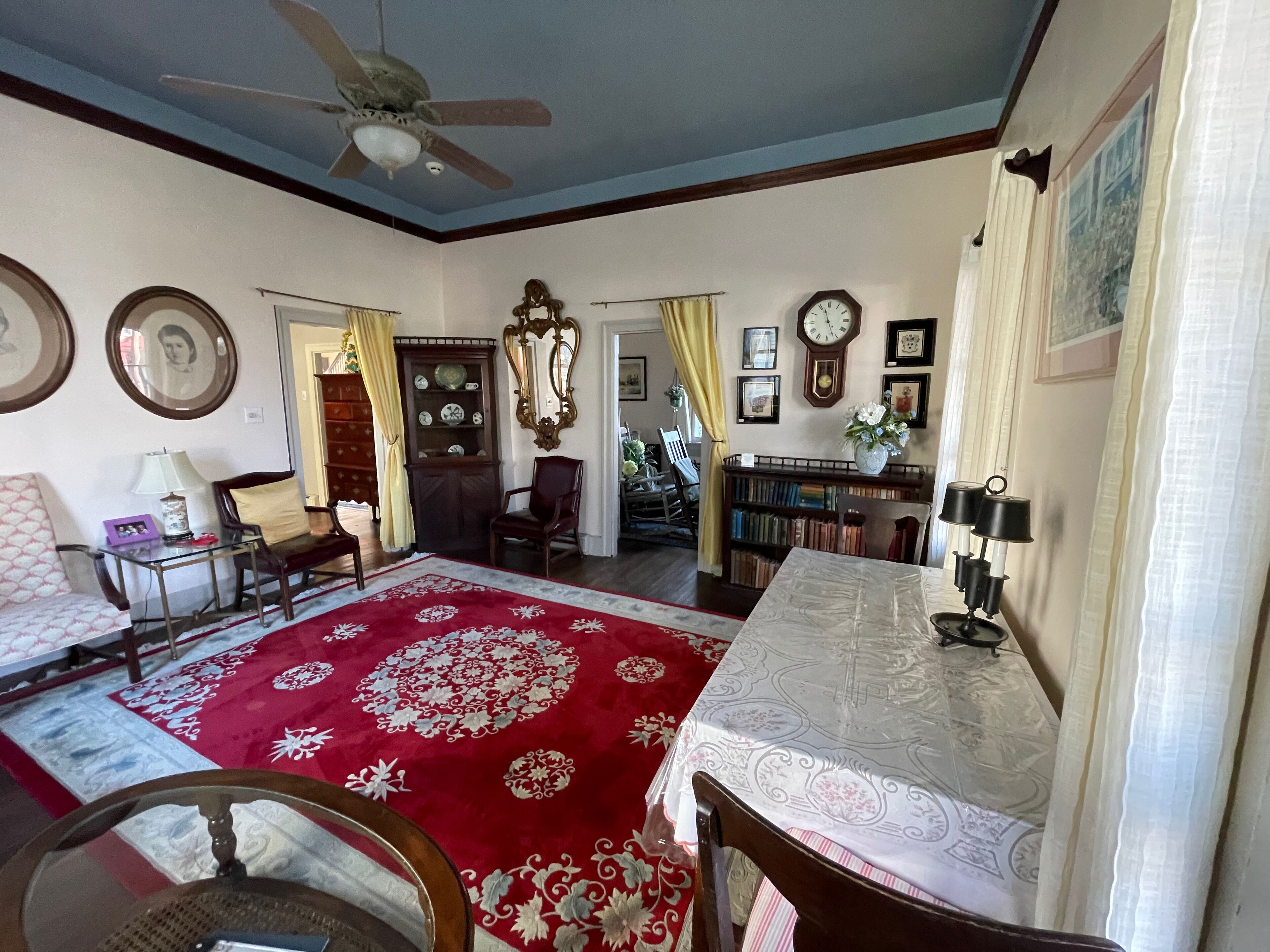 Un salon avec un tapis rouge à motifs, des meubles en bois, un ventilateur de plafond et une bibliothèque.