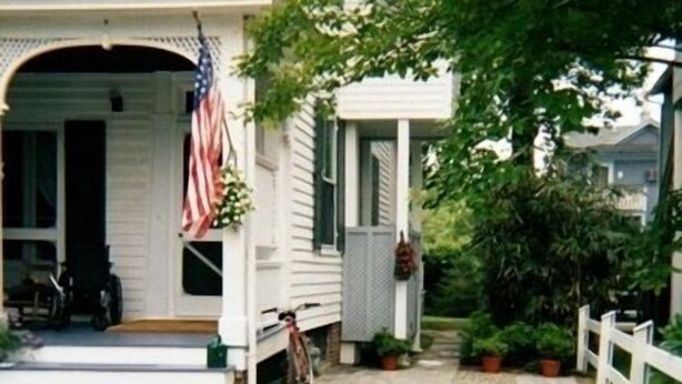 Una casa blanca con porche, una bandera estadounidense y una bicicleta.