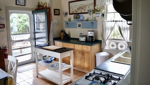Una cocina con estufa a gas, cafetera y ventana con cortinas.