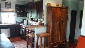 A kitchen with dark wooden cabinets, a granite countertop, and a built-in oven. There are two wooden stools and a large wooden cabinet with a curved top. - Bungalow 15 - Beachfront Pool View Private Gem! (Playa Hermosa)