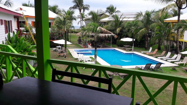 A pool area with lounge chairs and umbrellas, surrounded by palm trees and a thatched-roof structure. - Bungalow 15 - Beachfront Pool View Private Gem! (Playa Hermosa)