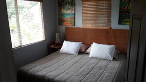 A bed with a patterned bedspread, two pillows, a nightstand with a lamp, and artwork on the walls. - Bungalow 15 - Beachfront Pool View Private Gem! (Playa Hermosa)