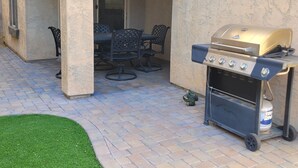 Eine Terrasse im Freien mit Grill, Gartenmöbeln und einer kleinen Rasenfläche.